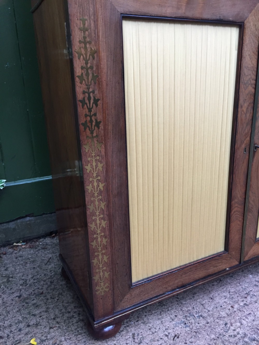 An early nineteenth-century Regency rosewood chiffonier featuring brass floral inlay, an upper shelf supported by brass columns, and twin cabinet doors with yellow pleated silk panels. View XI