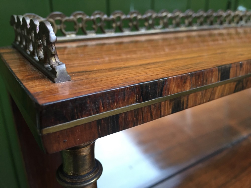 An early nineteenth-century Regency rosewood chiffonier featuring brass floral inlay, an upper shelf supported by brass columns, and twin cabinet doors with yellow pleated silk panels. View XII