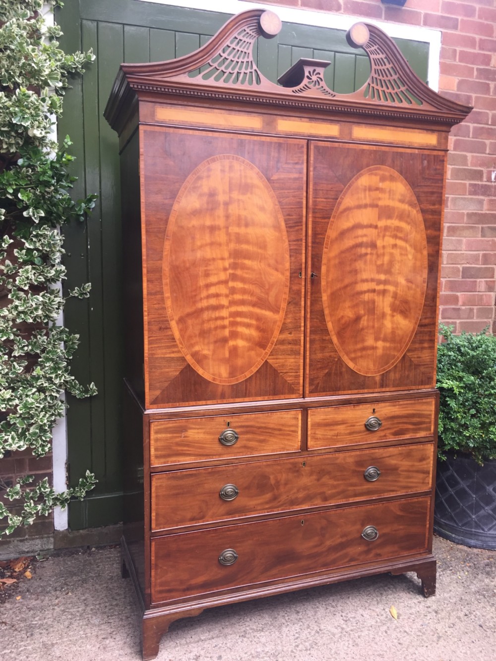 A late 18th-century George III mahogany and satinwood linen press with a swan-neck pediment, oval inlaid cupboard doors, and four lower drawers. View III