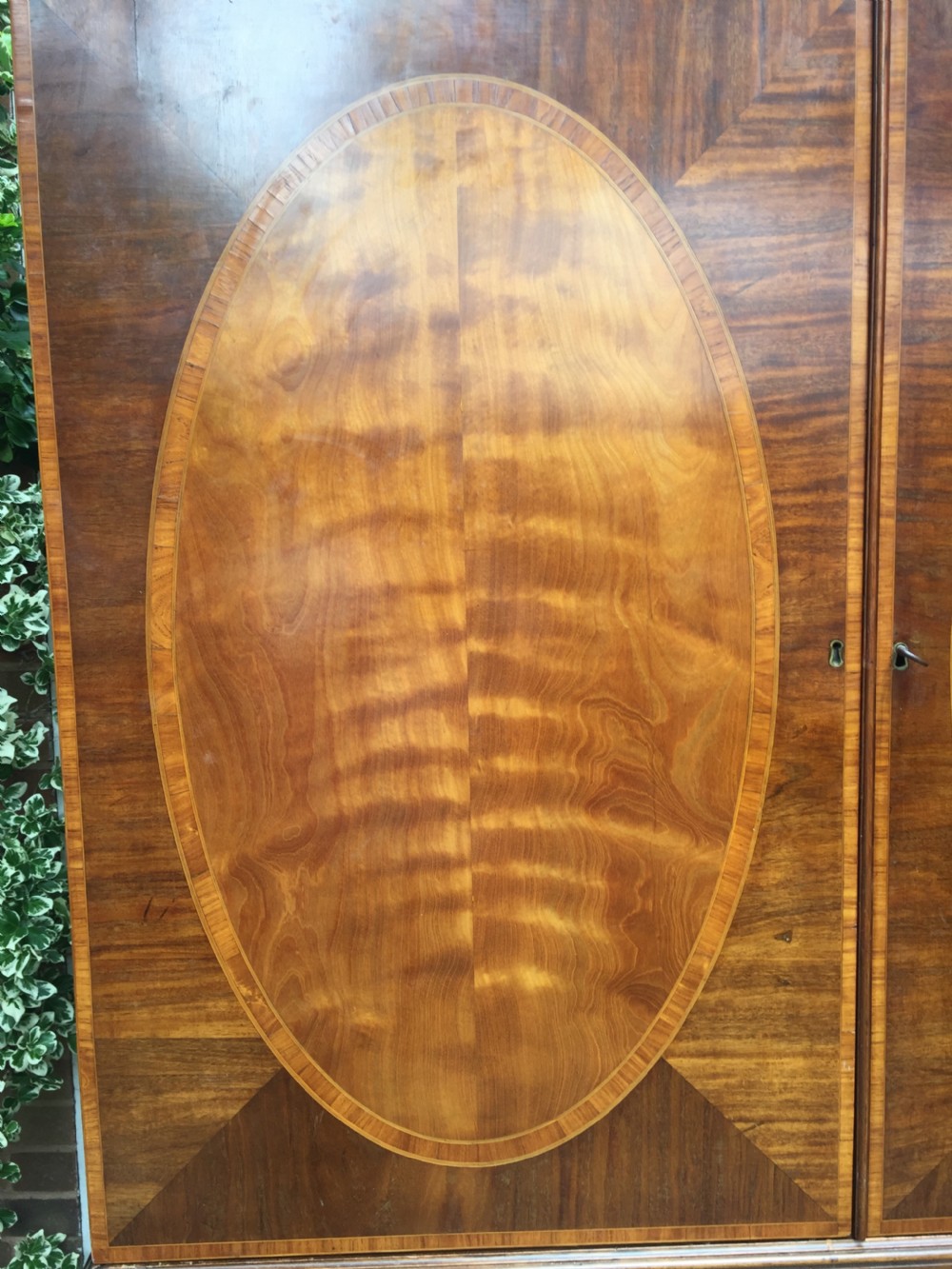 A late 18th-century George III mahogany and satinwood linen press with a swan-neck pediment, oval inlaid cupboard doors, and four lower drawers. View VII