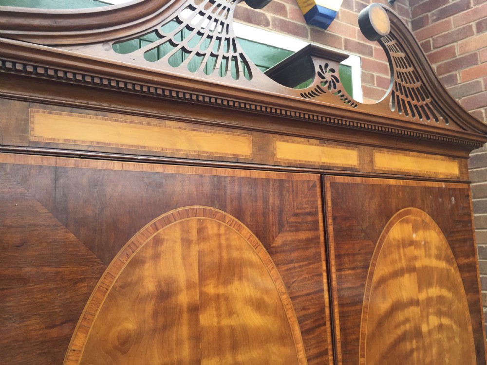 A late 18th-century George III mahogany and satinwood linen press with a swan-neck pediment, oval inlaid cupboard doors, and four lower drawers. View VIII