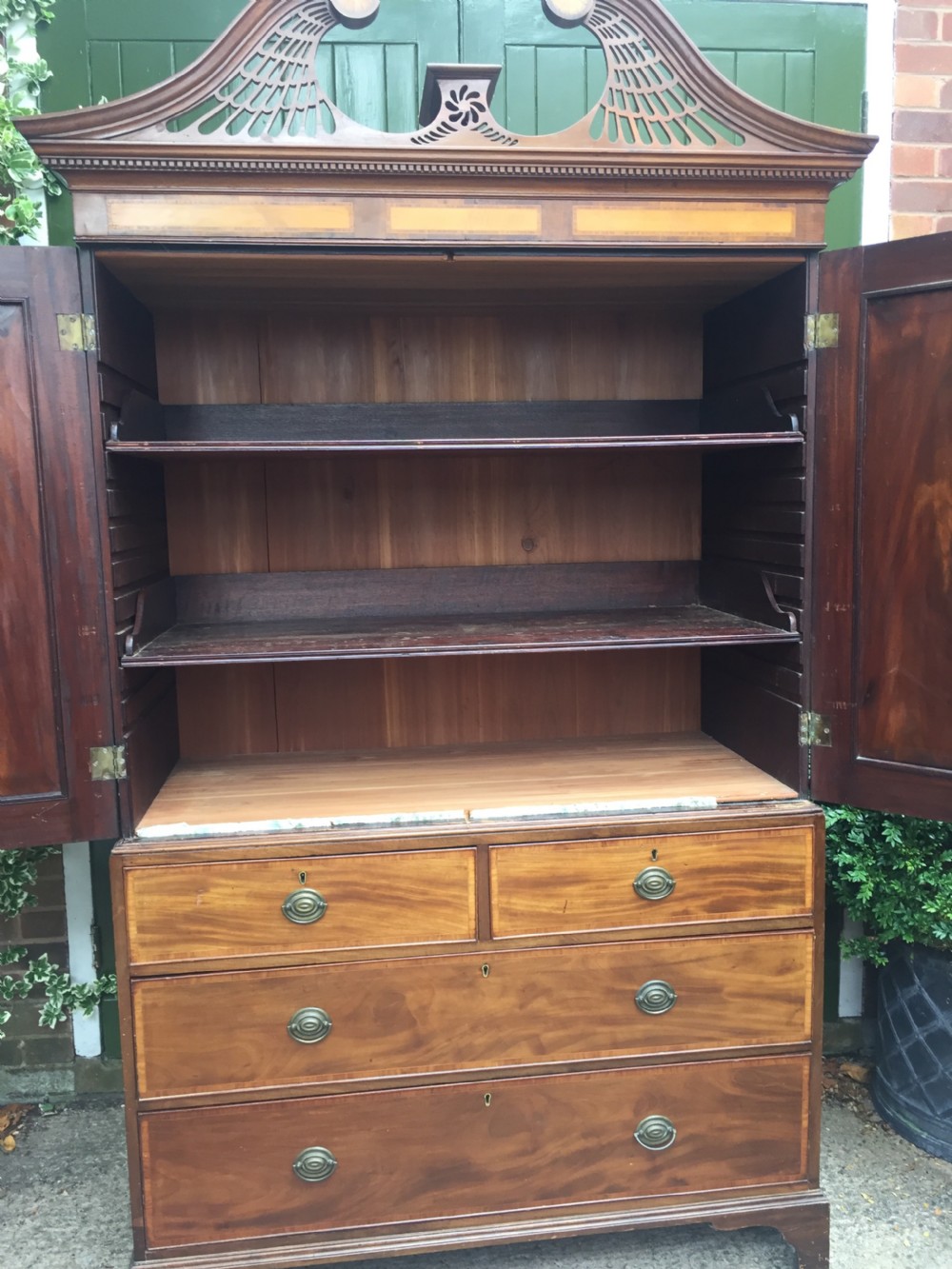 A late 18th-century George III mahogany and satinwood linen press with a swan-neck pediment, oval inlaid cupboard doors, and four lower drawers. View XIII