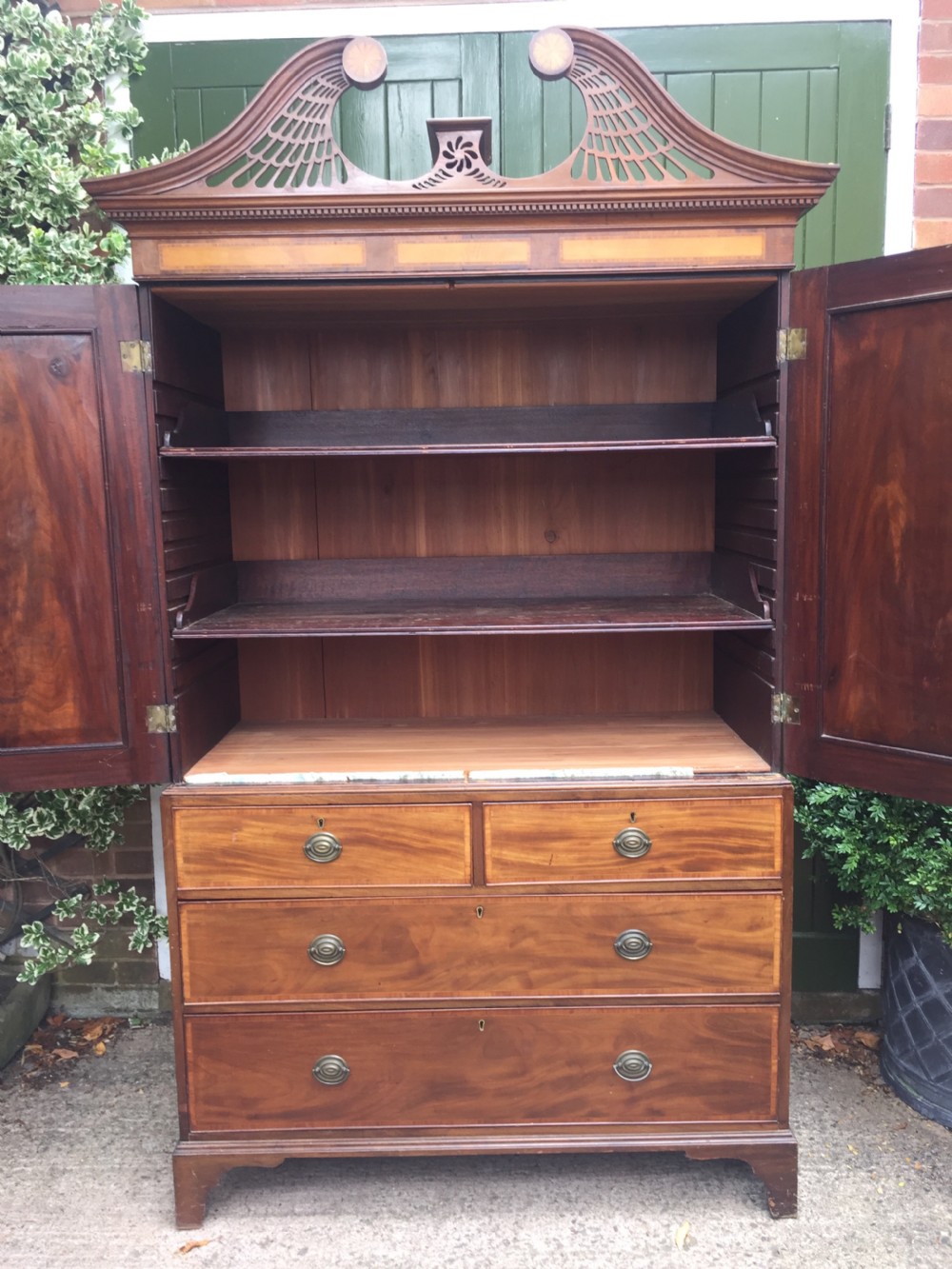A late 18th-century George III mahogany and satinwood linen press with a swan-neck pediment, oval inlaid cupboard doors, and four lower drawers. View XIV