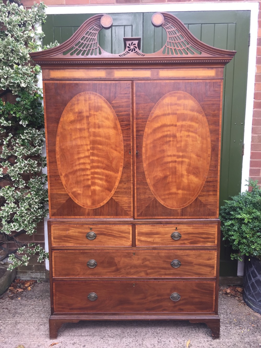 A late 18th-century George III mahogany and satinwood linen press with a swan-neck pediment, oval inlaid cupboard doors, and four lower drawers. View XXII