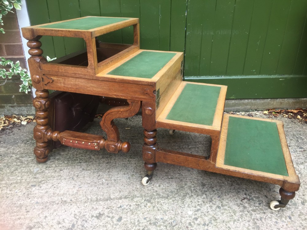 An early nineteenth-century carved oak metamorphic library armchair featuring a button-tufted leather backrest, caned seat, bobbin-turned details, and brass casters. View VI