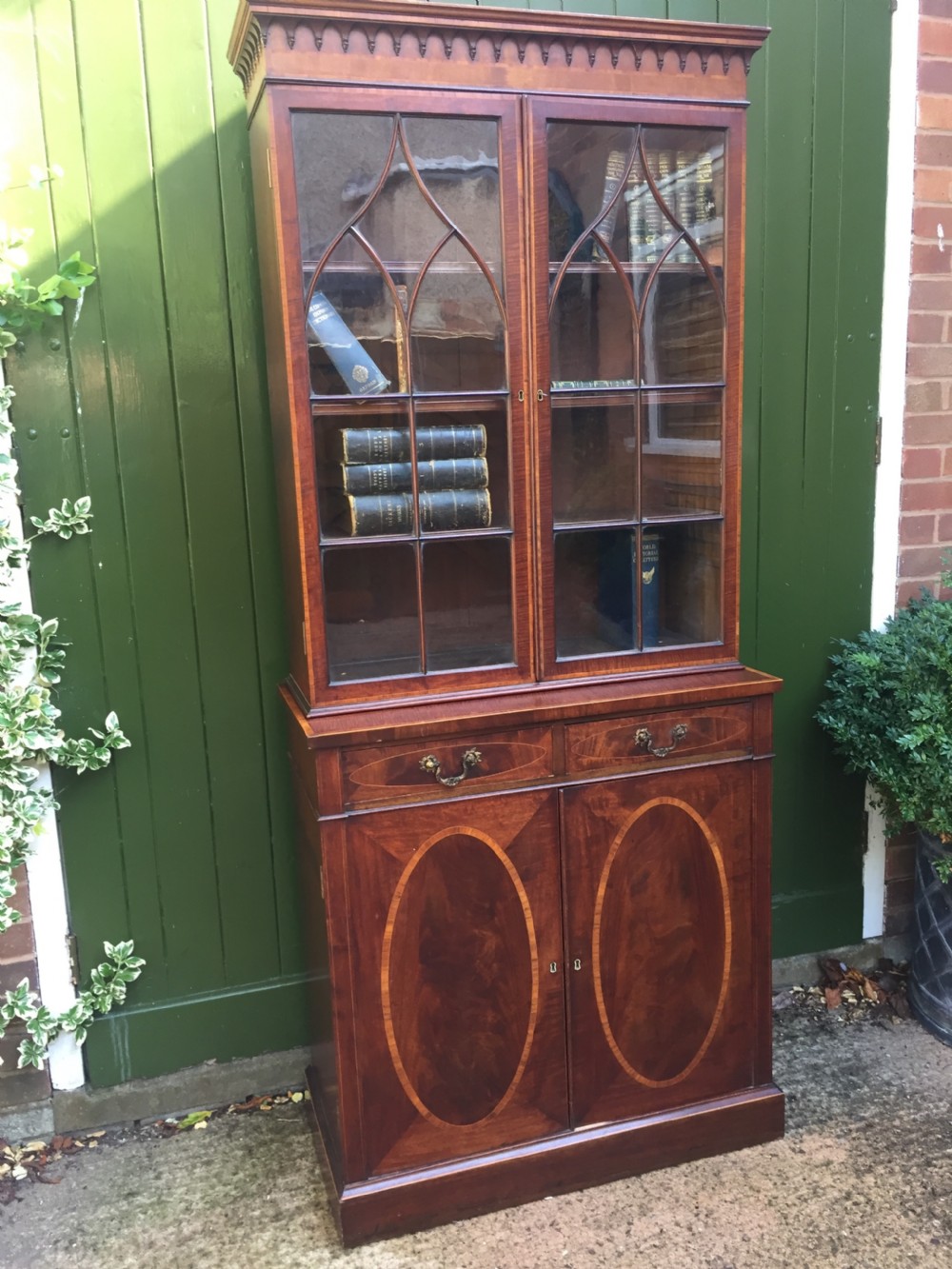 A late Victorian mahogany glazed cabinet featuring upper astragal doors with gothic tracery above two drawers and oval inlaid cupboard doors. View II