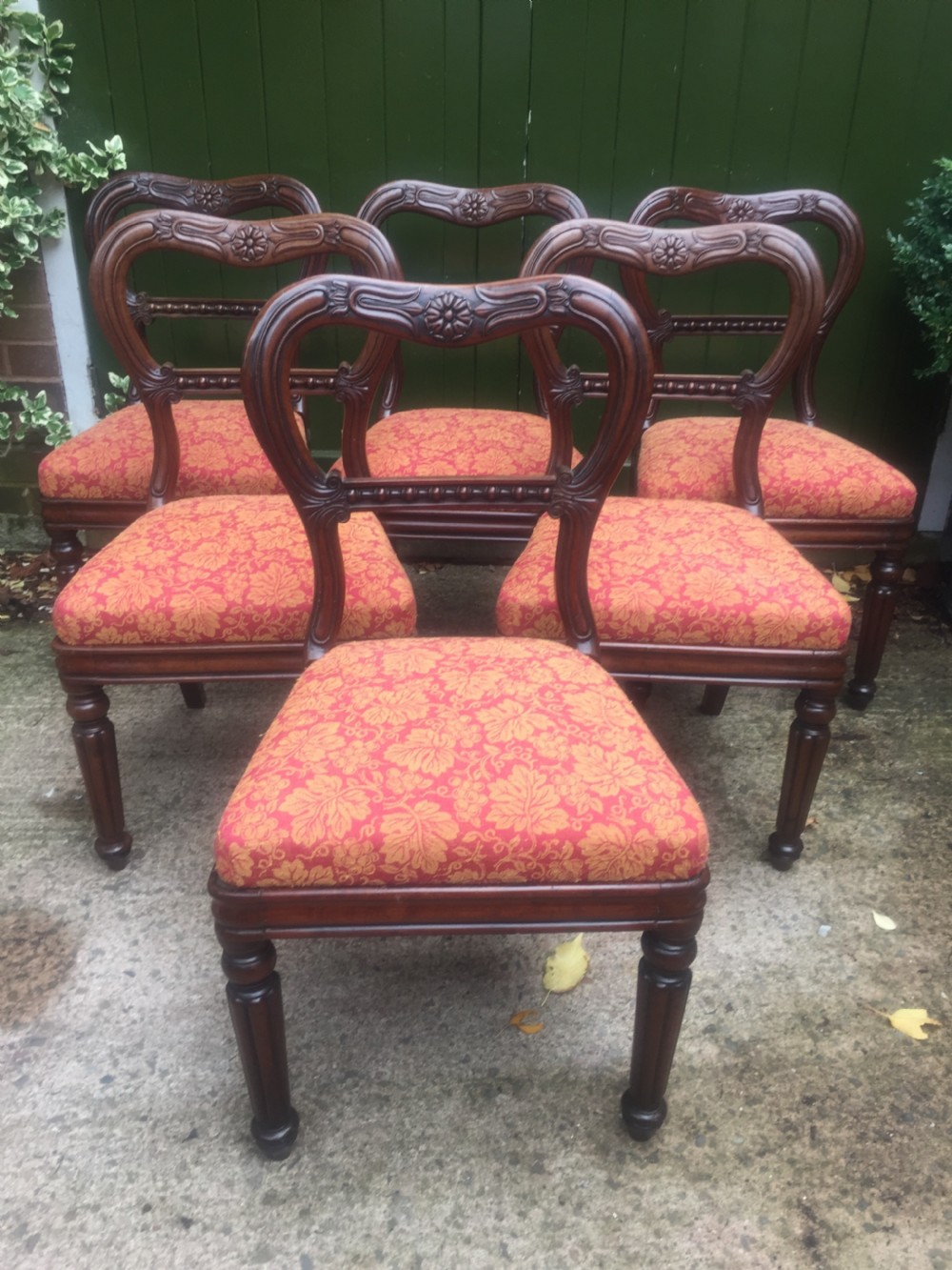 A set of six early nineteenth-century George IV mahogany dining chairs featuring carved balloon back frames, reeded legs, and red pattern upholstered seats.