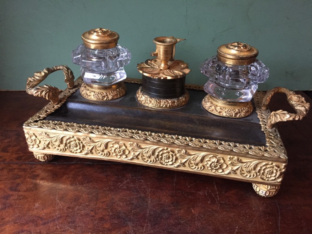 An early nineteenth-century French Empire style ormolu inkstand featuring two cut-crystal inkwells, a central holder, foliate handles, and a decorative gilt bronze tray.