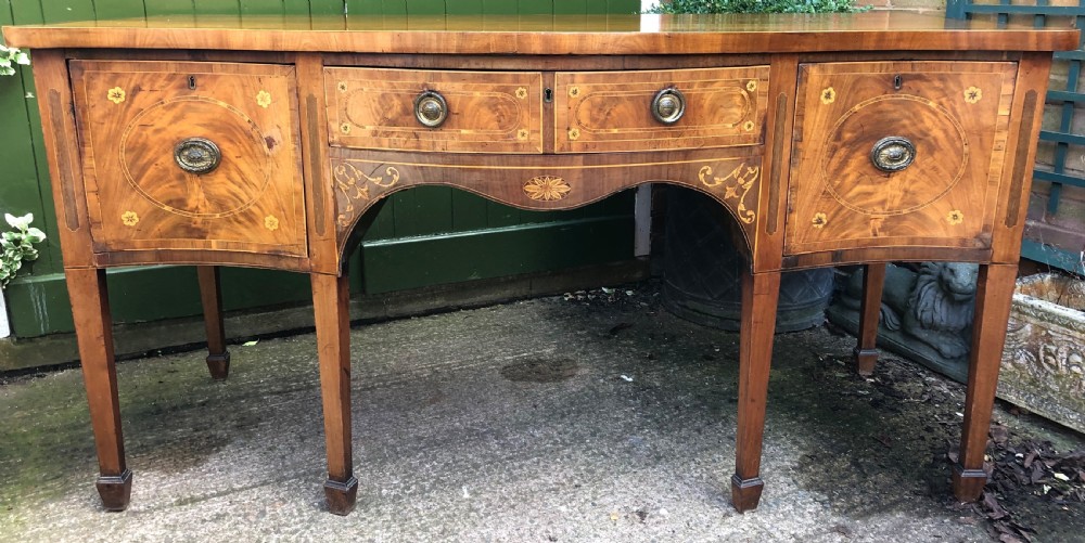 A late 18th-century George III mahogany sideboard featuring a serpentine front, floral marquetry inlay, tapering square legs with spade feet, and brass oval handles.