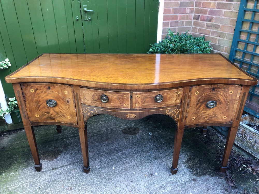 A late 18th-century George III mahogany sideboard featuring a serpentine front, floral marquetry inlay, tapering square legs with spade feet, and brass oval handles. View II
