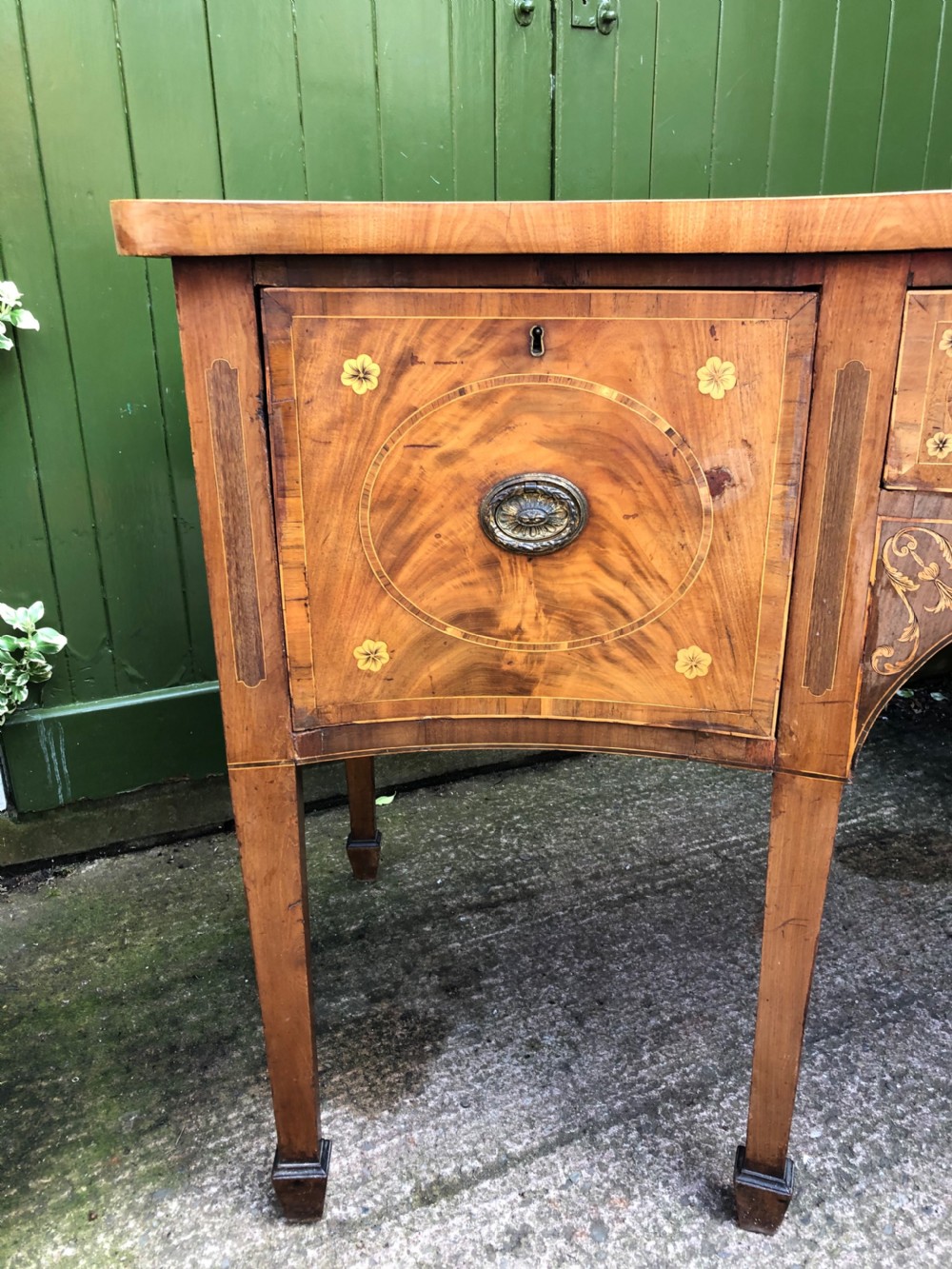A late 18th-century George III mahogany sideboard featuring a serpentine front, floral marquetry inlay, tapering square legs with spade feet, and brass oval handles. View III