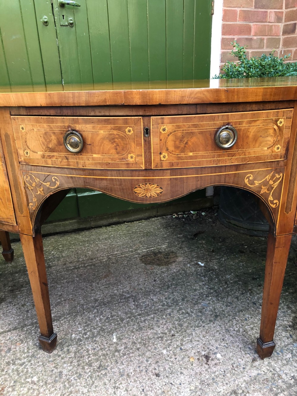 A late 18th-century George III mahogany sideboard featuring a serpentine front, floral marquetry inlay, tapering square legs with spade feet, and brass oval handles. View V