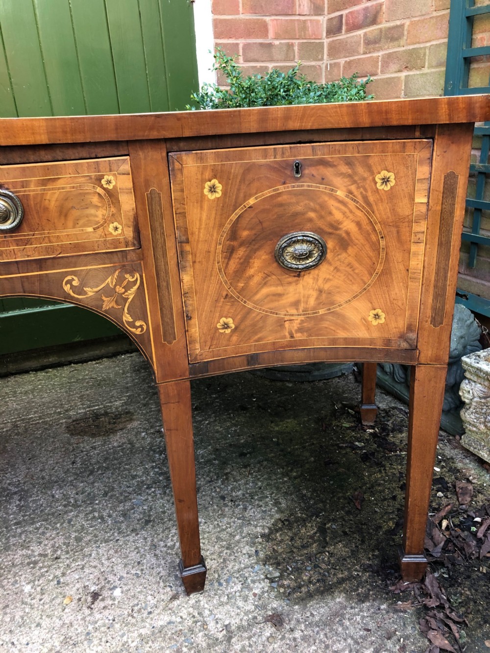 A late 18th-century George III mahogany sideboard featuring a serpentine front, floral marquetry inlay, tapering square legs with spade feet, and brass oval handles. View VI