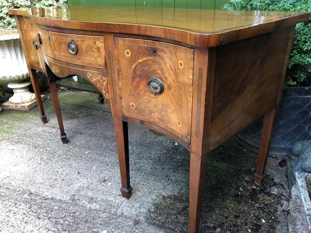A late 18th-century George III mahogany sideboard featuring a serpentine front, floral marquetry inlay, tapering square legs with spade feet, and brass oval handles. View XIII