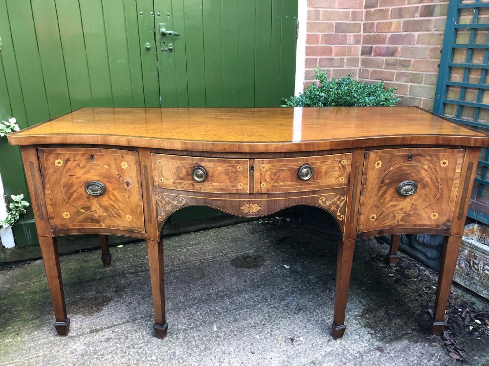A late 18th-century George III mahogany sideboard featuring a serpentine front, floral marquetry inlay, tapering square legs with spade feet, and brass oval handles. View XV