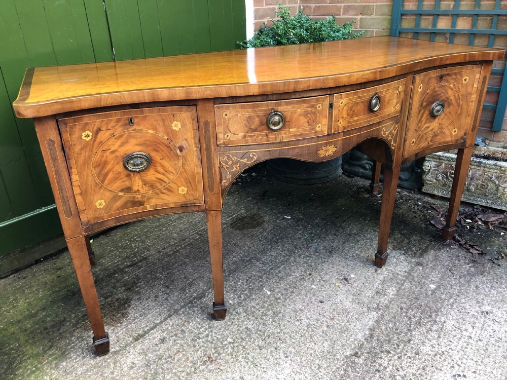 A late 18th-century George III mahogany sideboard featuring a serpentine front, floral marquetry inlay, tapering square legs with spade feet, and brass oval handles. View XVI