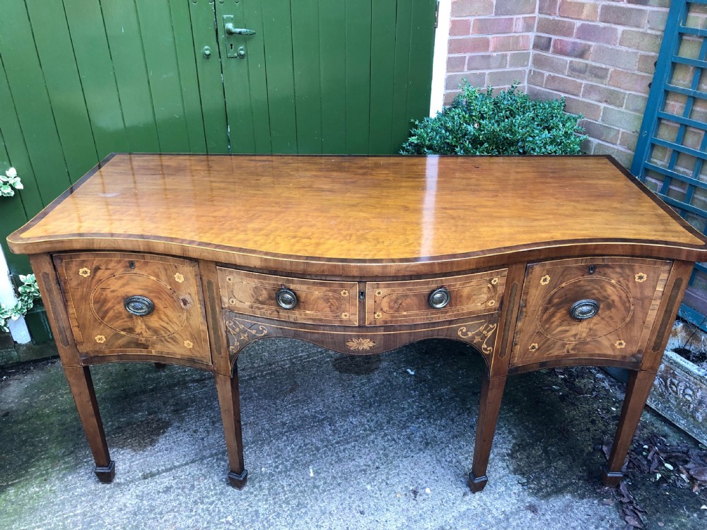 A late 18th-century George III mahogany sideboard featuring a serpentine front, floral marquetry inlay, tapering square legs with spade feet, and brass oval handles. View XVII