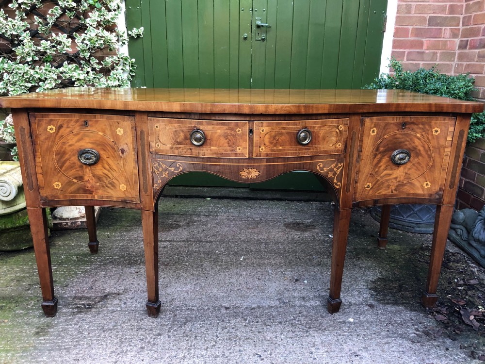 A late 18th-century George III mahogany sideboard featuring a serpentine front, floral marquetry inlay, tapering square legs with spade feet, and brass oval handles. View XXV