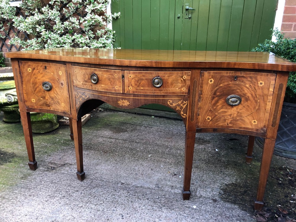 A late 18th-century George III mahogany sideboard featuring a serpentine front, floral marquetry inlay, tapering square legs with spade feet, and brass oval handles. View XXVII