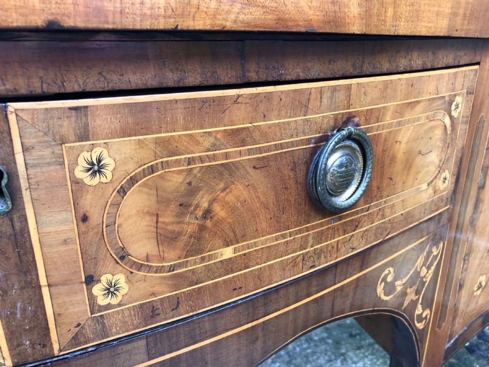 A late 18th-century George III mahogany sideboard featuring a serpentine front, floral marquetry inlay, tapering square legs with spade feet, and brass oval handles. View XXVIII