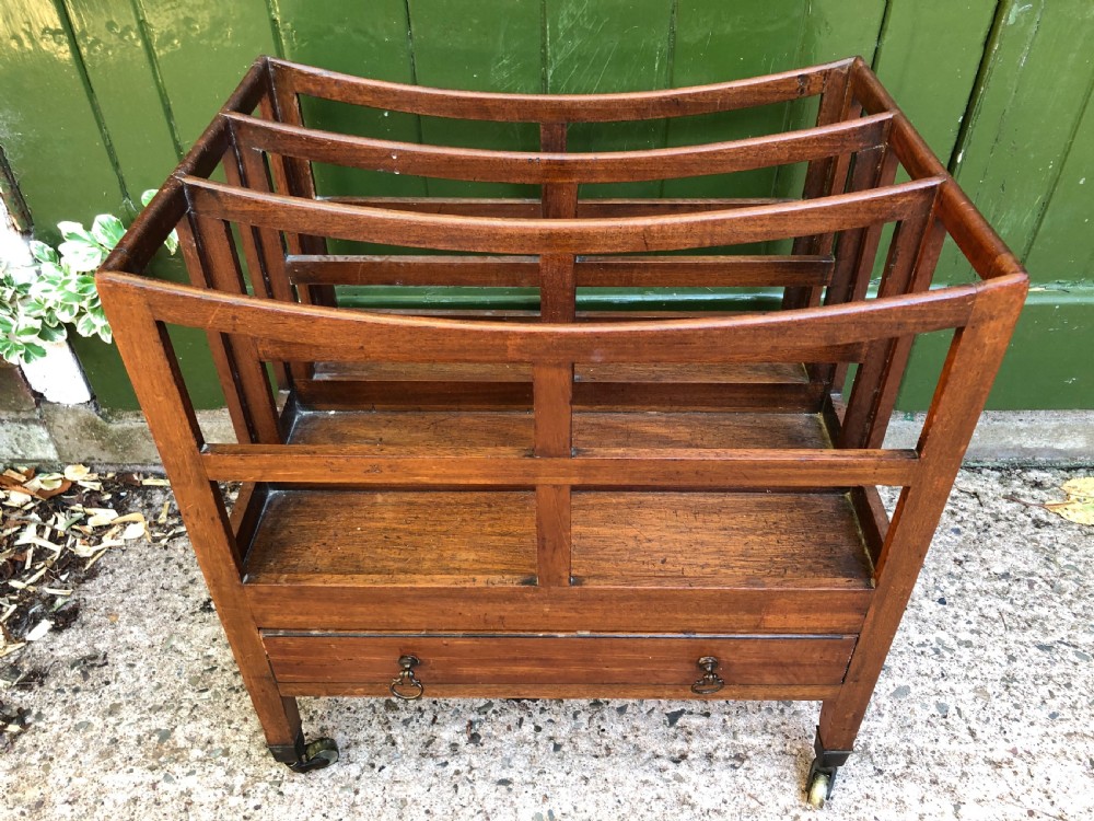 A late George III mahogany canterbury featuring slatted dividers, a concave top crest rail, a single base drawer with brass knobs, and square legs ending in brass castors. View III