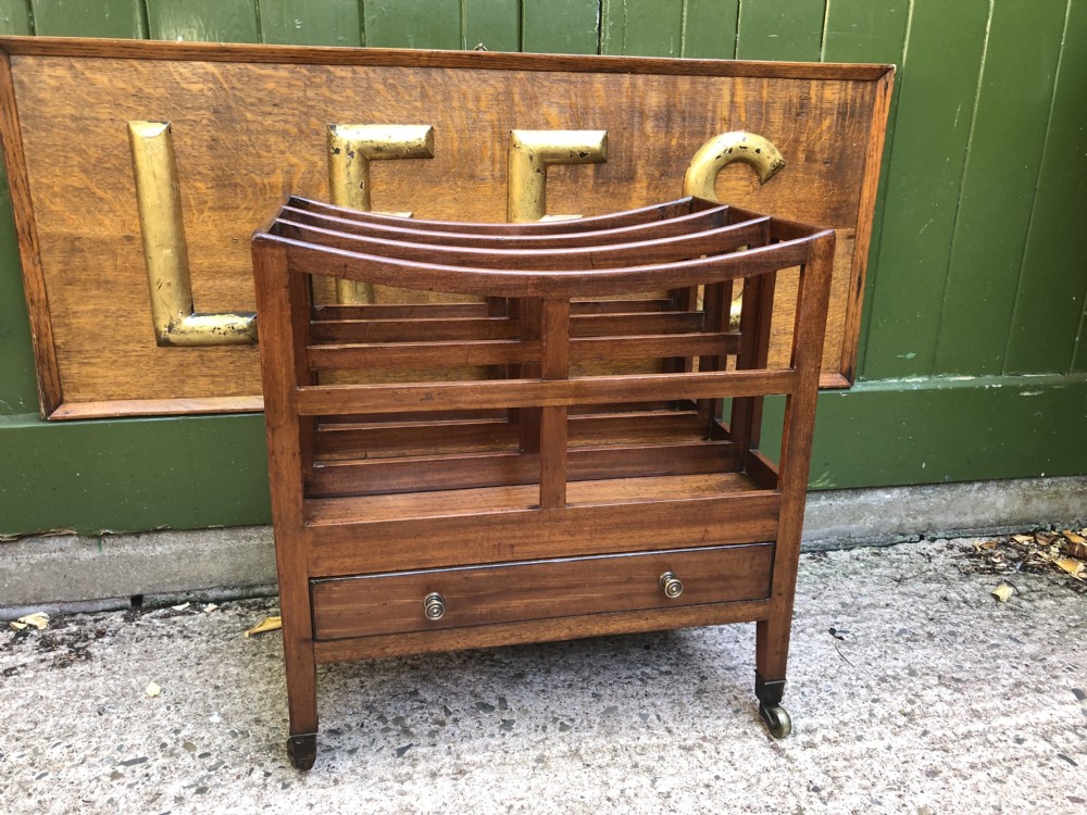 A late George III mahogany canterbury featuring slatted dividers, a concave top crest rail, a single base drawer with brass knobs, and square legs ending in brass castors. View II