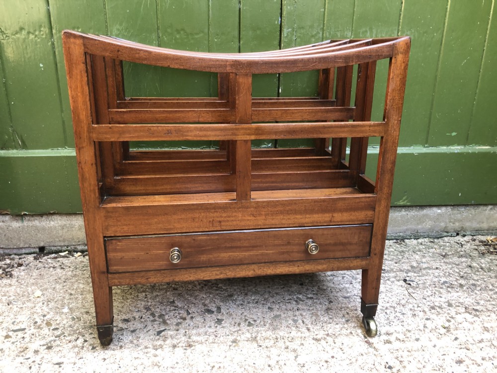A late George III mahogany canterbury featuring slatted dividers, a concave top crest rail, a single base drawer with brass knobs, and square legs ending in brass castors. View V