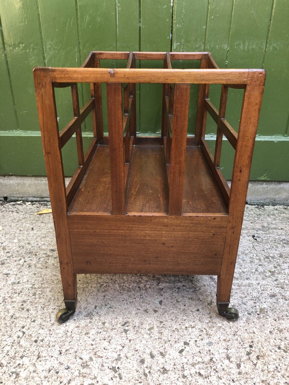 A late George III mahogany canterbury featuring slatted dividers, a concave top crest rail, a single base drawer with brass knobs, and square legs ending in brass castors. View VI