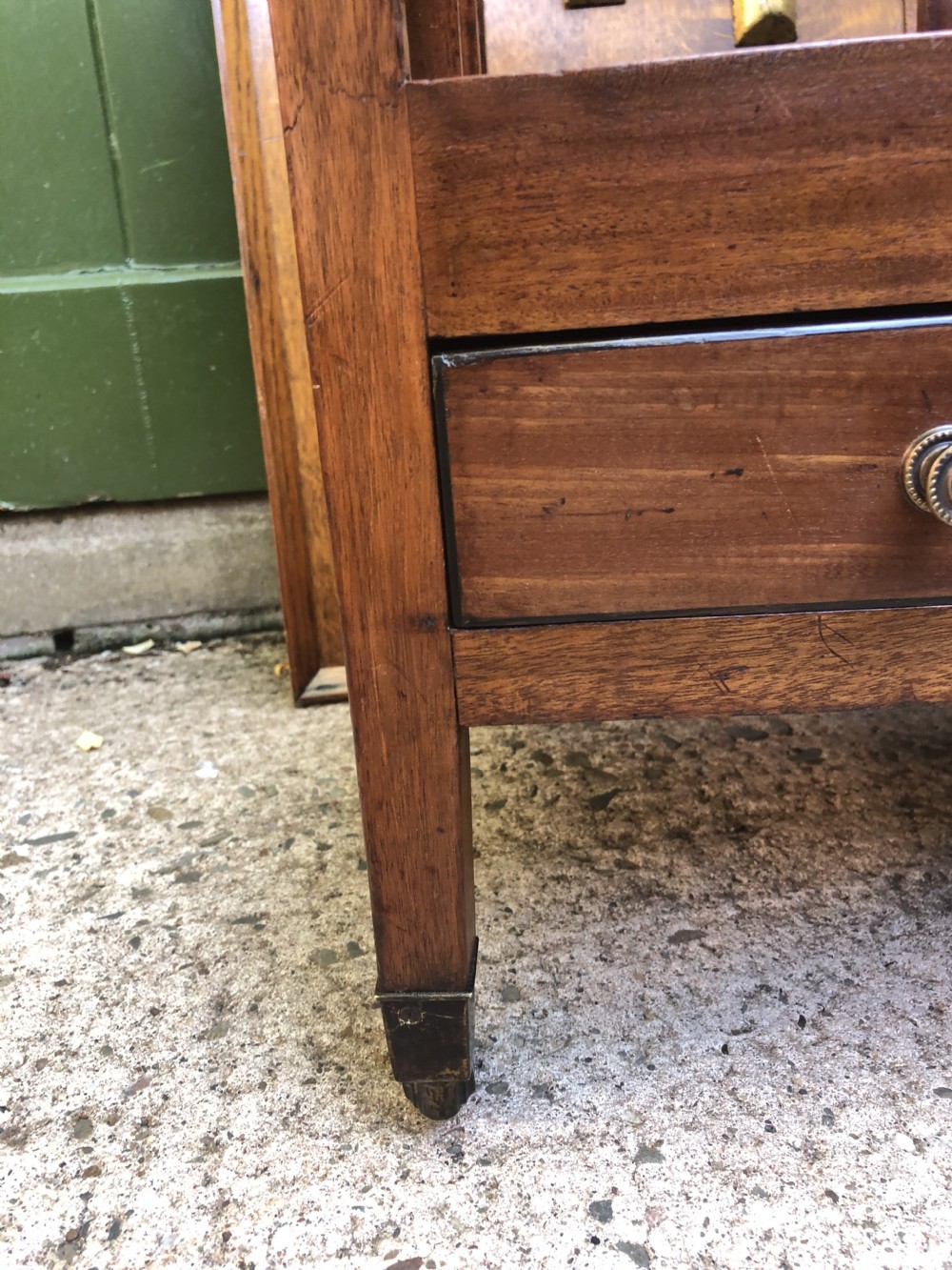 A late George III mahogany canterbury featuring slatted dividers, a concave top crest rail, a single base drawer with brass knobs, and square legs ending in brass castors. View XI