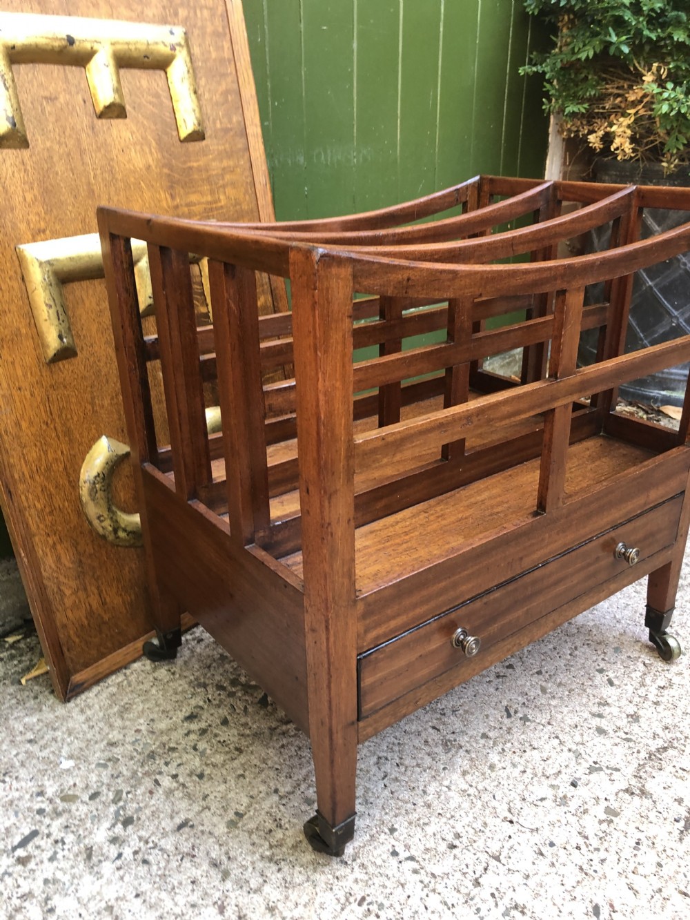 A late George III mahogany canterbury featuring slatted dividers, a concave top crest rail, a single base drawer with brass knobs, and square legs ending in brass castors. View XIII