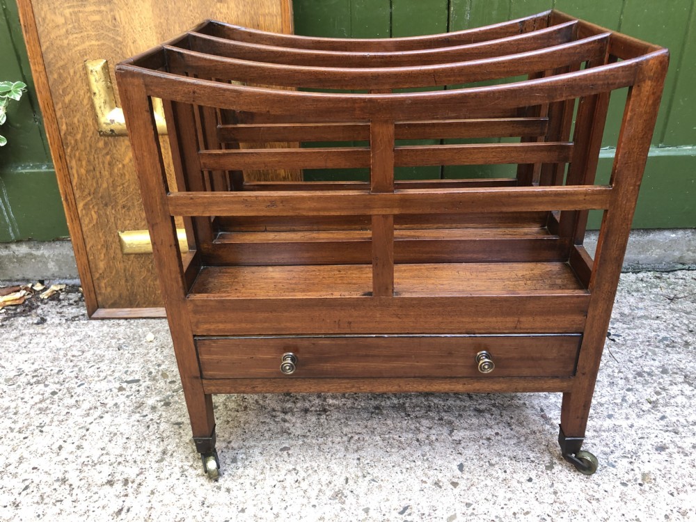 A late George III mahogany canterbury featuring slatted dividers, a concave top crest rail, a single base drawer with brass knobs, and square legs ending in brass castors. View XV