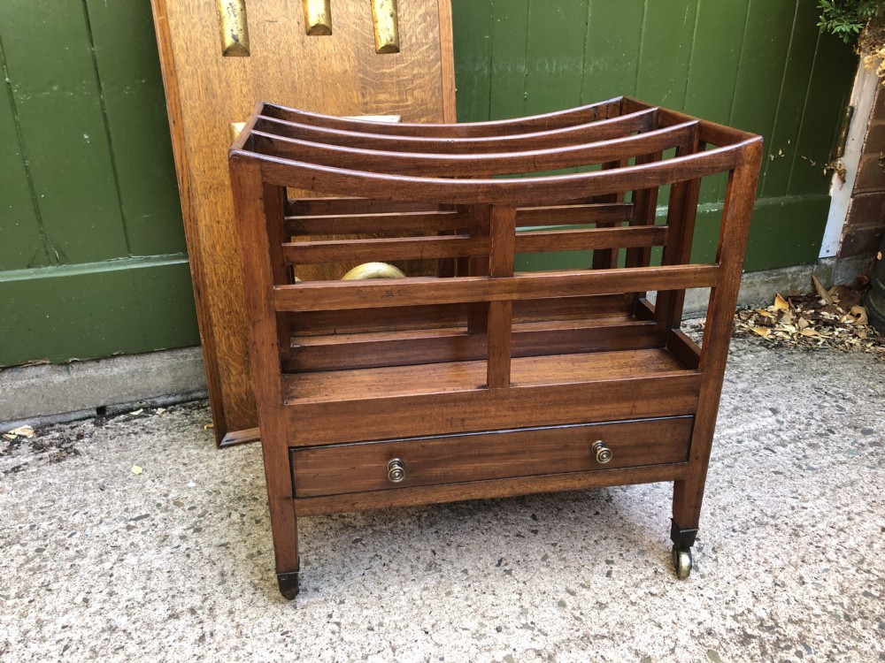 A late George III mahogany canterbury featuring slatted dividers, a concave top crest rail, a single base drawer with brass knobs, and square legs ending in brass castors. View XVI