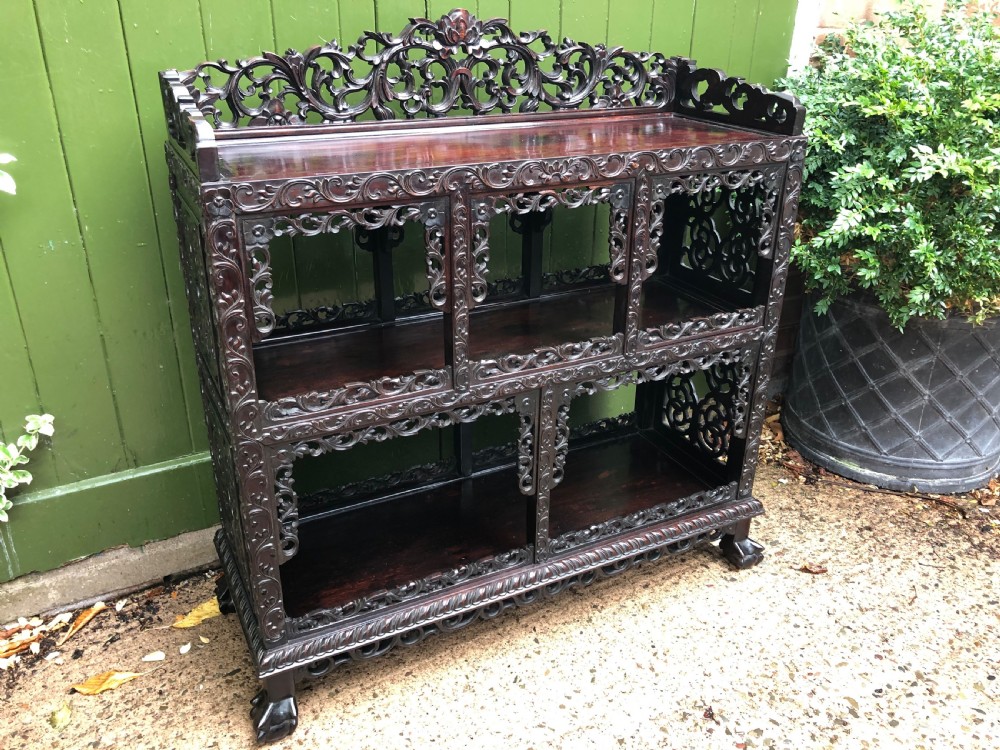 A dark rosewood late nineteenth-century Chinese display cabinet featuring intricate openwork carving throughout tiered open shelves and a crest rail. View XIX