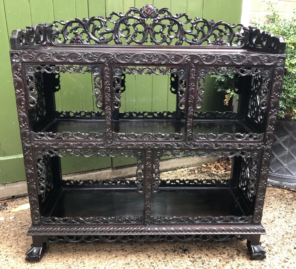 A dark rosewood late nineteenth-century Chinese display cabinet featuring intricate openwork carving throughout tiered open shelves and a crest rail.
