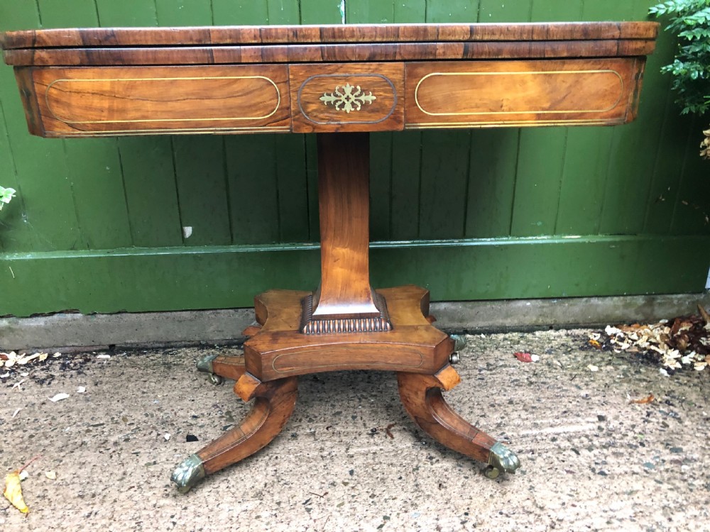 An early nineteenth-century Regency rosewood fold-over card table featuring decorative brass line inlay, a central pedestal, and splayed legs with brass claw feet. View II