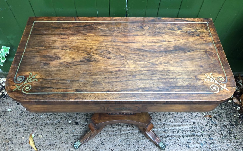 An early nineteenth-century Regency rosewood fold-over card table featuring decorative brass line inlay, a central pedestal, and splayed legs with brass claw feet. View III