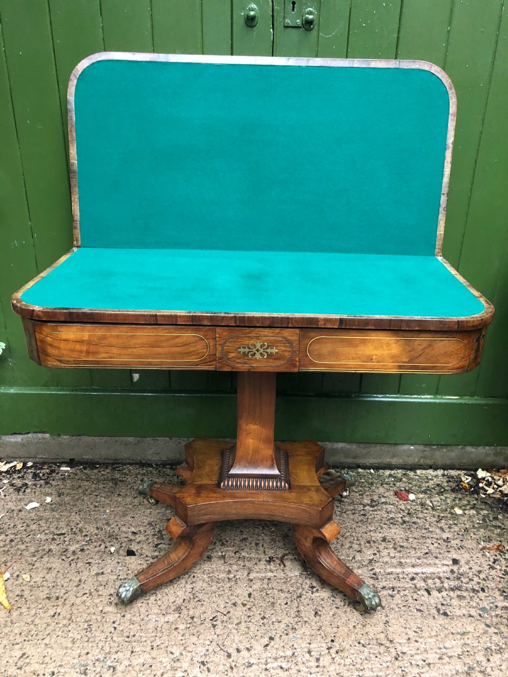 An early nineteenth-century Regency rosewood fold-over card table featuring decorative brass line inlay, a central pedestal, and splayed legs with brass claw feet. View X