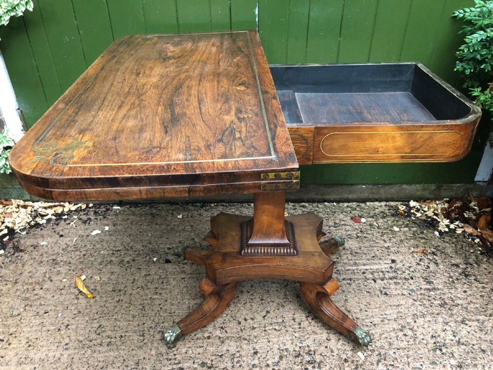 An early nineteenth-century Regency rosewood fold-over card table featuring decorative brass line inlay, a central pedestal, and splayed legs with brass claw feet. View XII