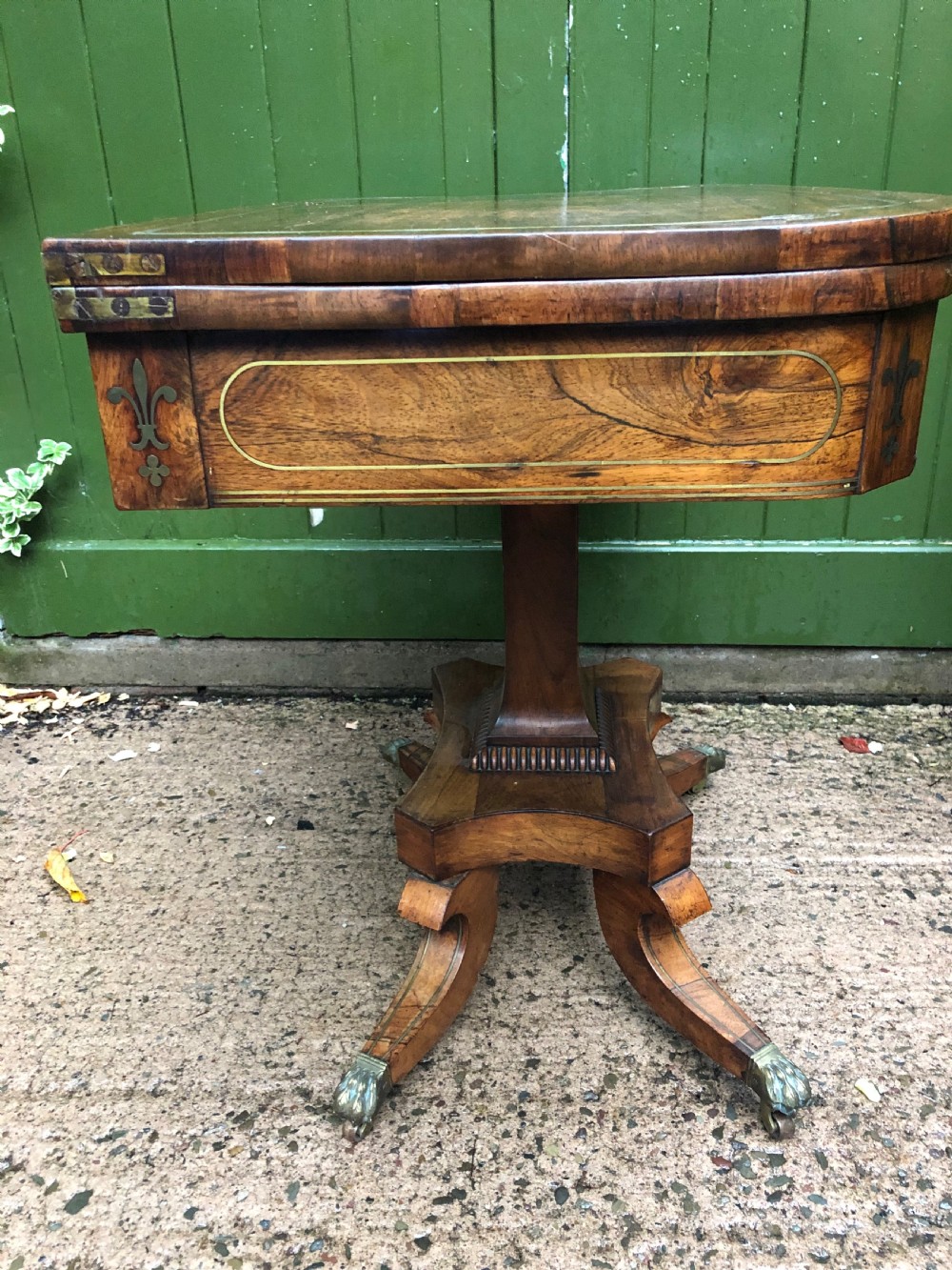 An early nineteenth-century Regency rosewood fold-over card table featuring decorative brass line inlay, a central pedestal, and splayed legs with brass claw feet. View XIV