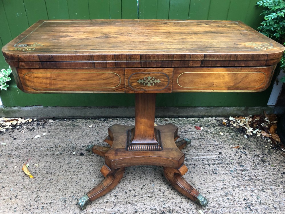An early nineteenth-century Regency rosewood fold-over card table featuring decorative brass line inlay, a central pedestal, and splayed legs with brass claw feet. View XVII