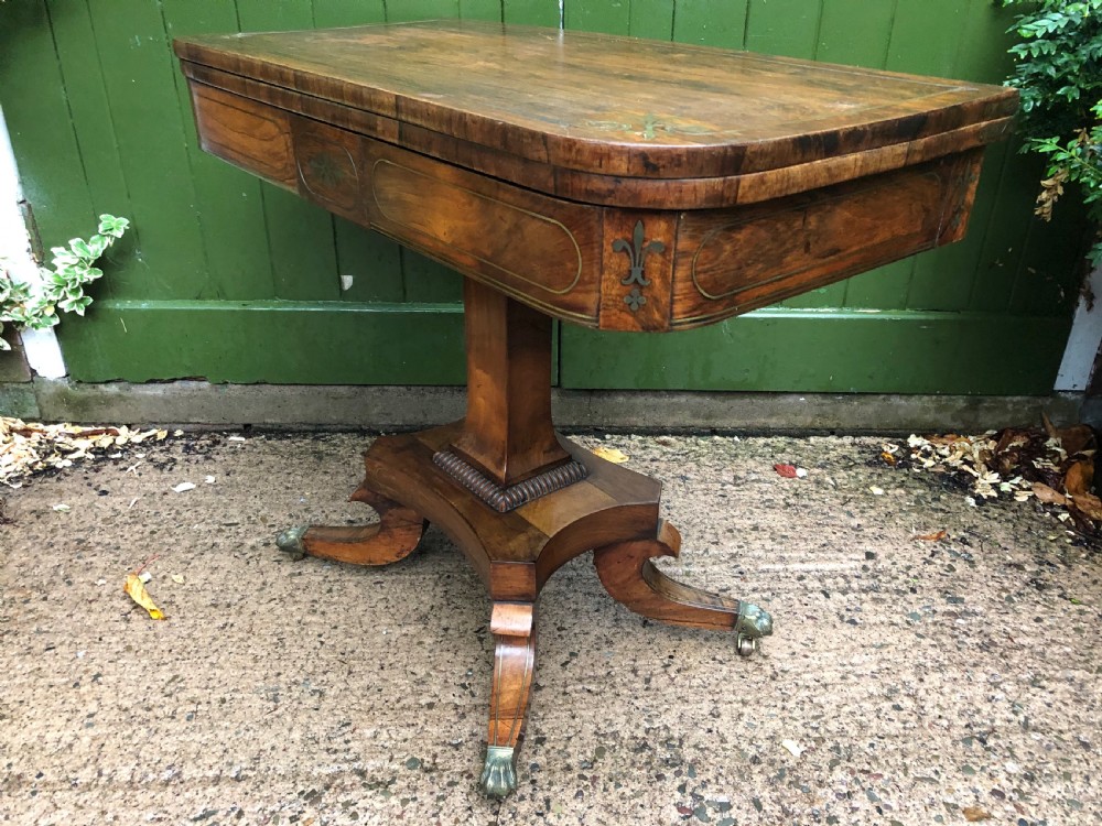 An early nineteenth-century Regency rosewood fold-over card table featuring decorative brass line inlay, a central pedestal, and splayed legs with brass claw feet. View XVIII