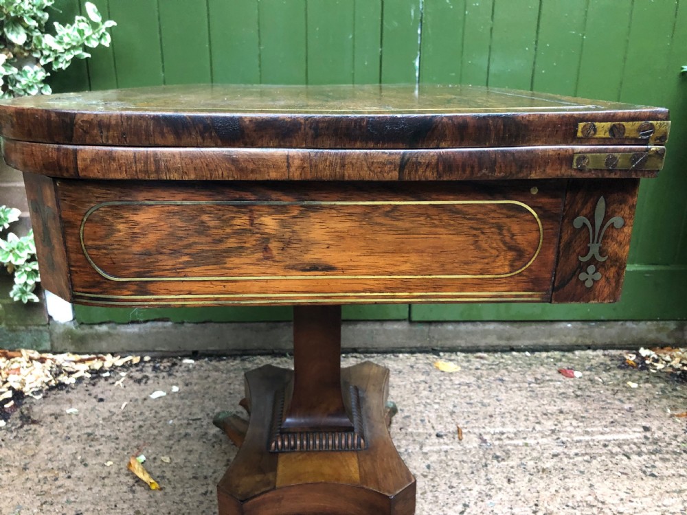 An early nineteenth-century Regency rosewood fold-over card table featuring decorative brass line inlay, a central pedestal, and splayed legs with brass claw feet. View XIX