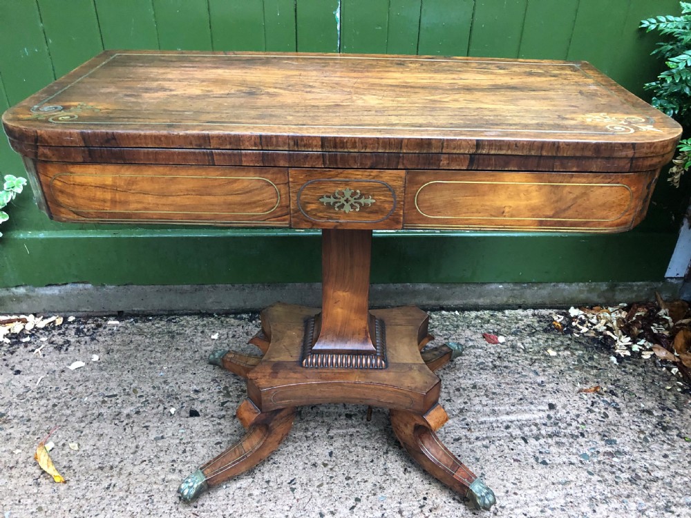 An early nineteenth-century Regency rosewood fold-over card table featuring decorative brass line inlay, a central pedestal, and splayed legs with brass claw feet. View XXII