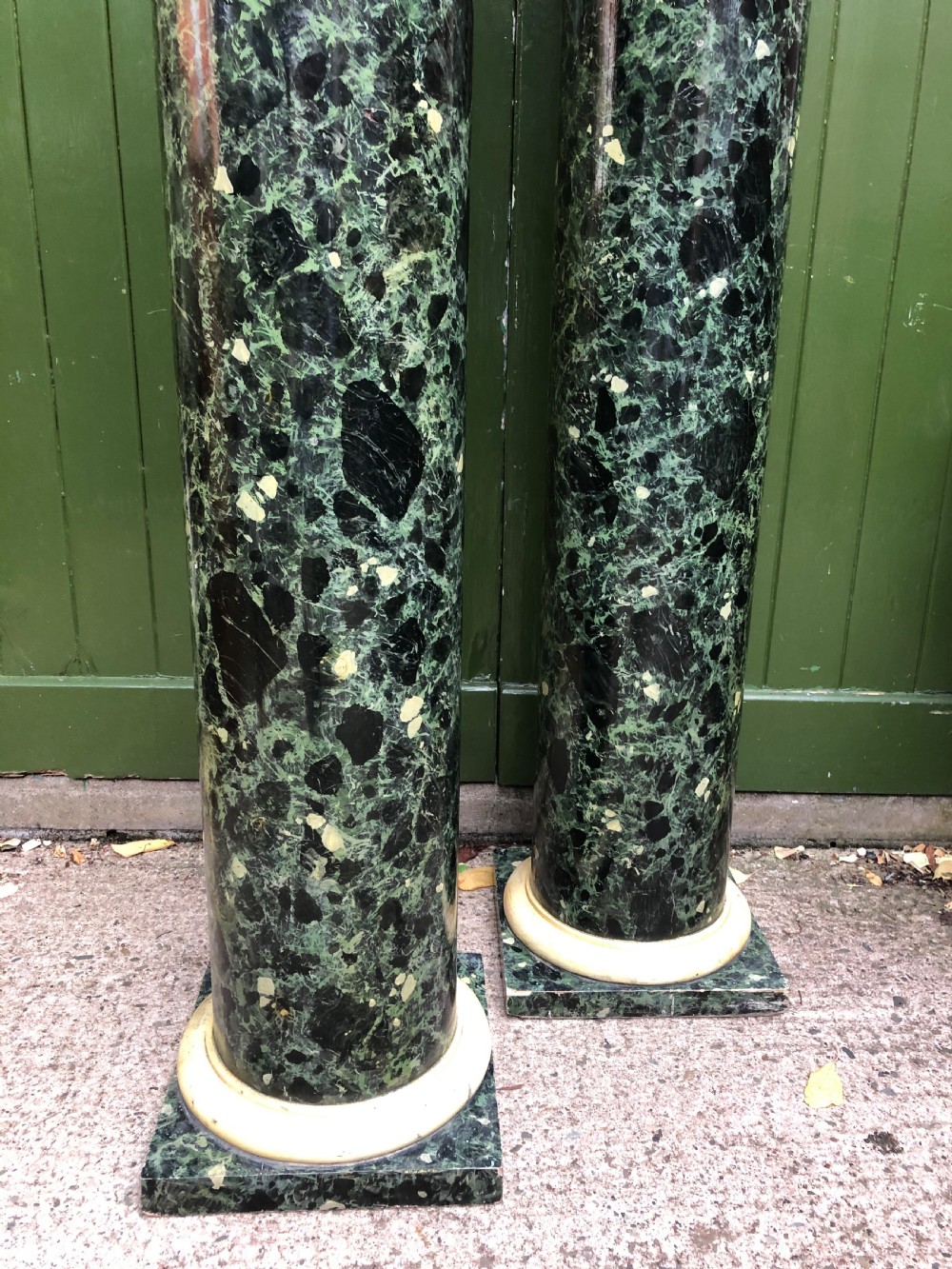 A pair of tall mid-19th century cylindrical wooden display columns painted in a green and black faux verde antico marble finish with square bases. View XX