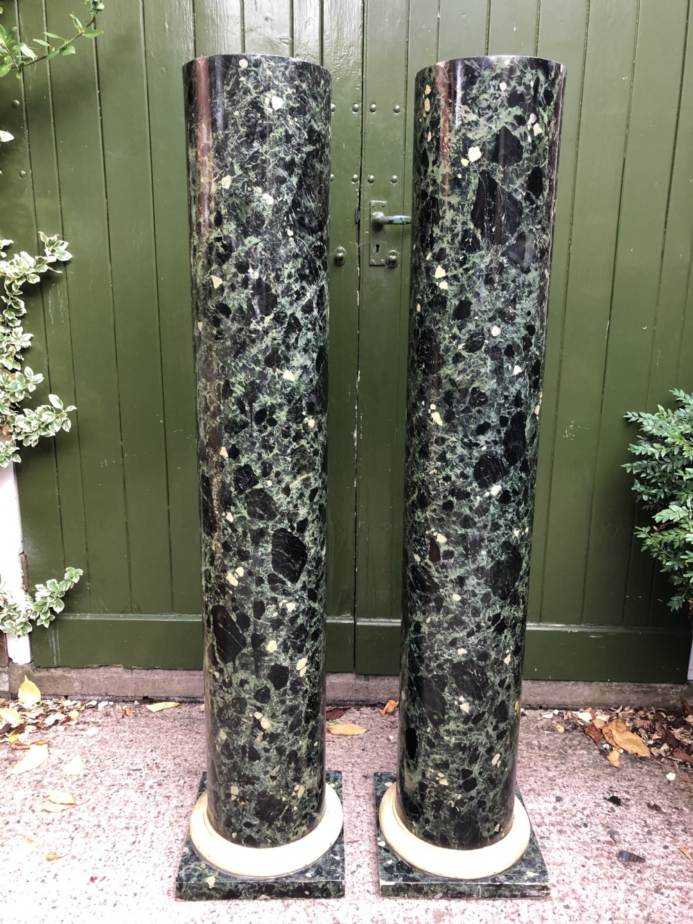 A pair of tall mid-19th century cylindrical wooden display columns painted in a green and black faux verde antico marble finish with square bases.