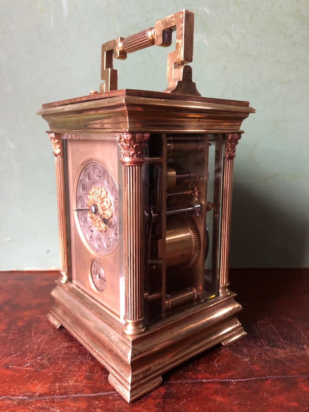 A late nineteenth-century French gilt brass carriage clock featuring fluted Corinthian corner columns, a carrying handle, a central dial with Arabic numerals, a lower subsidiary dial, and an adjacent winding key. View VII