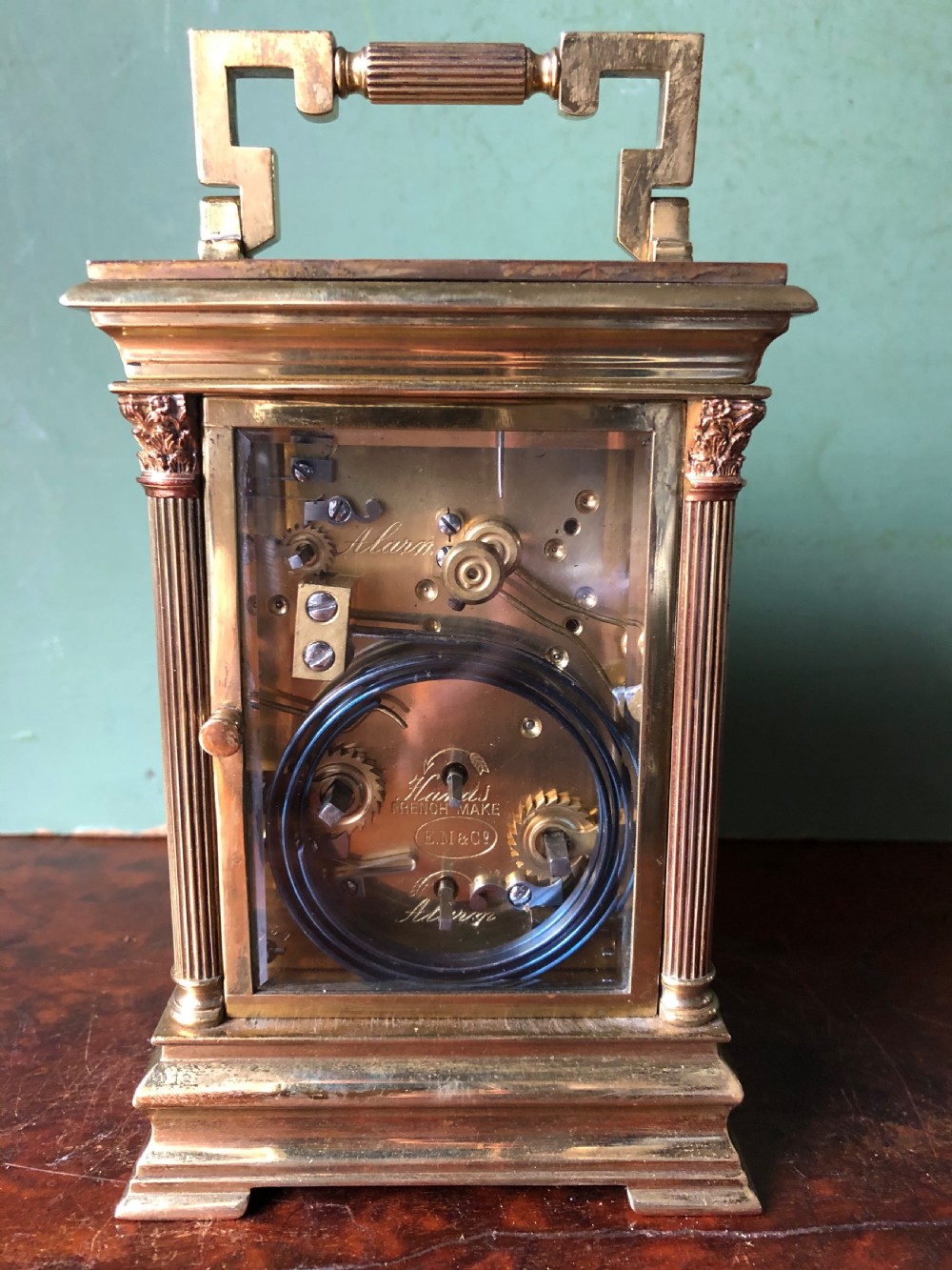 A late nineteenth-century French gilt brass carriage clock featuring fluted Corinthian corner columns, a carrying handle, a central dial with Arabic numerals, a lower subsidiary dial, and an adjacent winding key. View X
