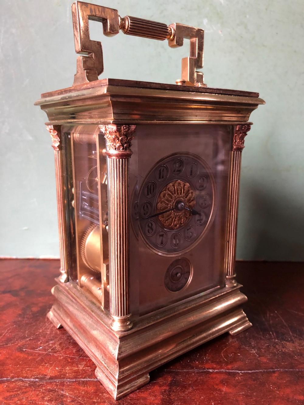 A late nineteenth-century French gilt brass carriage clock featuring fluted Corinthian corner columns, a carrying handle, a central dial with Arabic numerals, a lower subsidiary dial, and an adjacent winding key. View XI