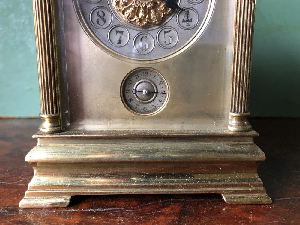 A late nineteenth-century French gilt brass carriage clock featuring fluted Corinthian corner columns, a carrying handle, a central dial with Arabic numerals, a lower subsidiary dial, and an adjacent winding key. View XII