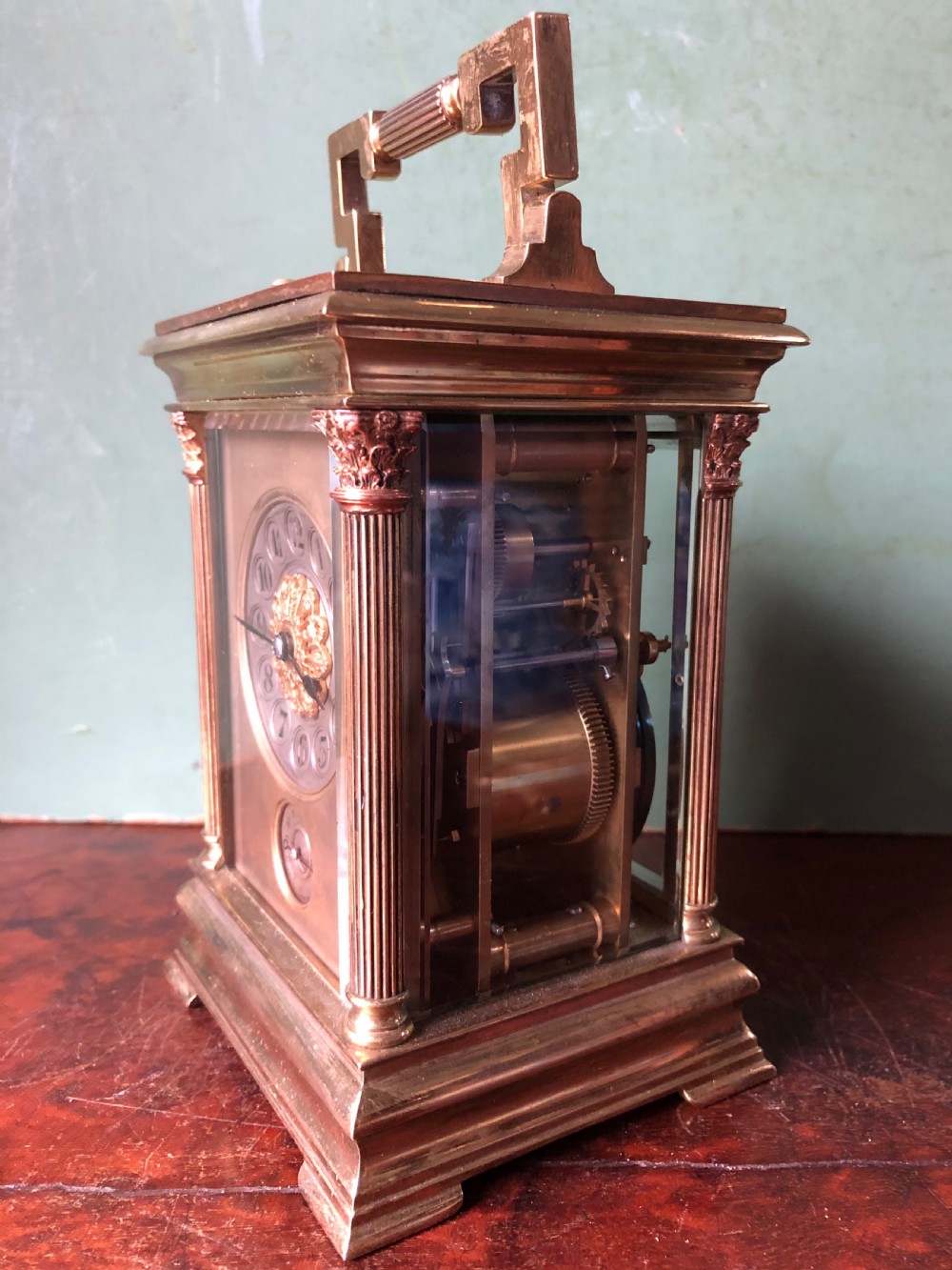 A late nineteenth-century French gilt brass carriage clock featuring fluted Corinthian corner columns, a carrying handle, a central dial with Arabic numerals, a lower subsidiary dial, and an adjacent winding key. View XVI